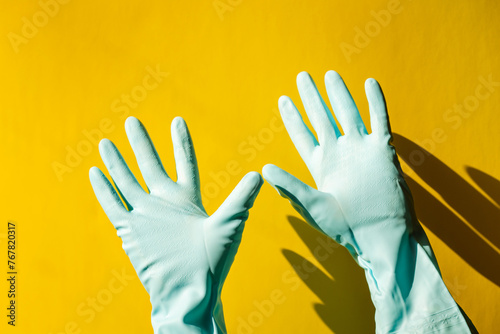 house cleaning concept. hands in blue rubber household raised up and waving on yellow background. © Natalia