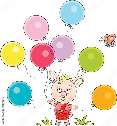 Funny cartoony little piglet playing with colorful toy balloons and merry butterfly on a green summer lawn in a park, vector cartoon illustration on a white background