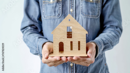 Person dressed in denim holds a small wooden house model, concept of home ownership photo