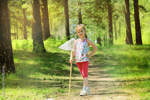 Fototapeta Naklejka Na Ścianę i Meble -  Cute little girl walking and catching butterflies with her scoop-net on sunny summer day