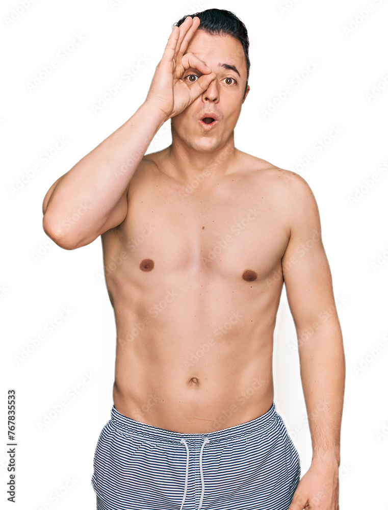 Fototapeta premium Handsome young man wearing swimwear shirtless doing ok gesture shocked with surprised face, eye looking through fingers. unbelieving expression.