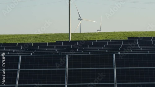 Solar panels in the background of a green hill and rotating wind turbines