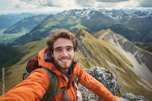 A young male hiker, smiling, taking a selfie on a mountain peak.