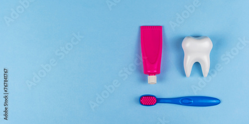 The health of children's teeth. White healthy tooth and baby toothpaste and brush on a blue background. A concept for a dental clinic, a pediatric dentist, oral hygiene, oral care. Copyspace for text