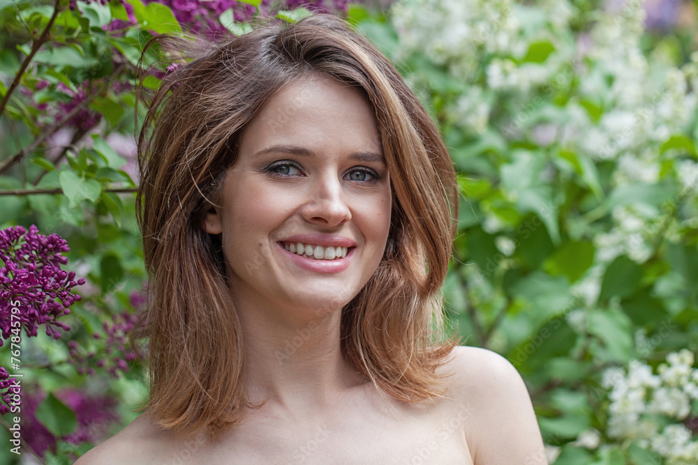 Joyful young adult brunette female model with fresh clean skin, bob haircut and natural makeup against green blurred leaves background with white spring flower Joyful young adult brunette female model with fresh clean skin, bob haircut and natural makeup against green blurred leaves background with white spring flower