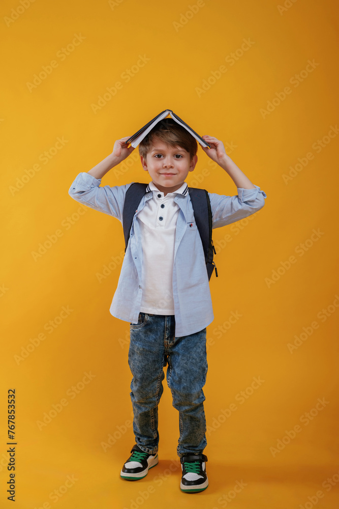 Book is above the head, having fun. Little boy is in the studio against yellow background