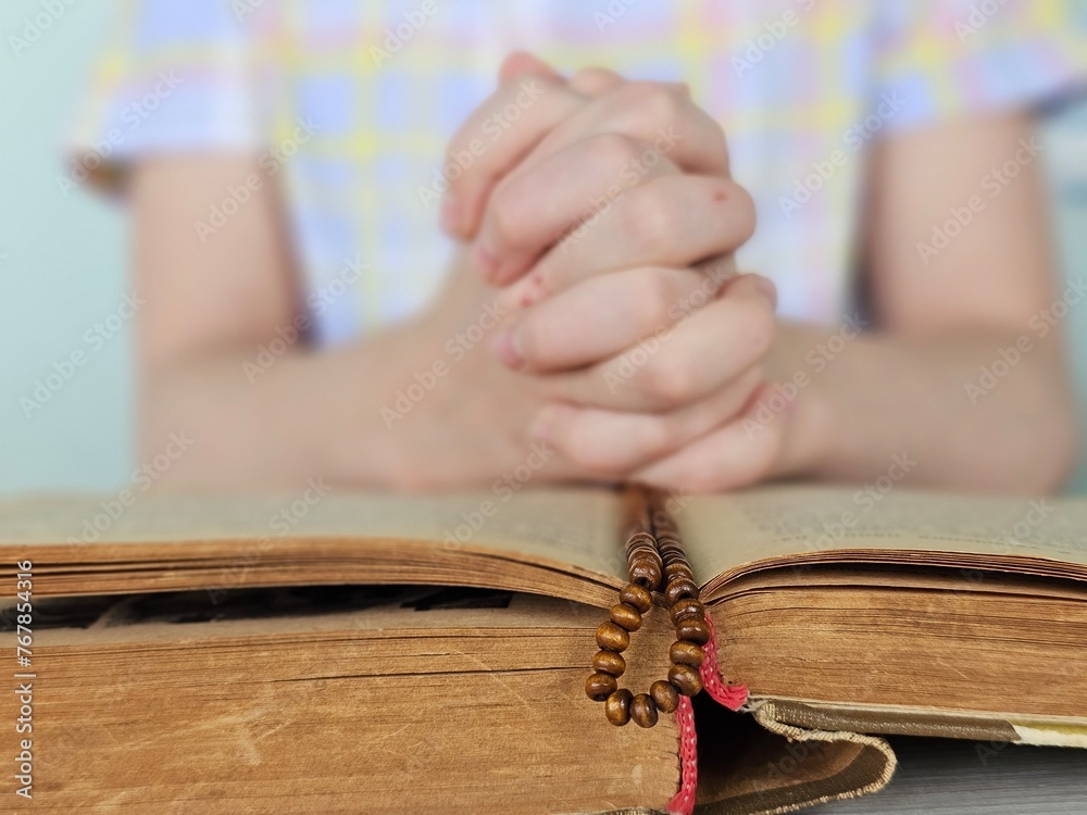 Obraz premium Hands of praying boy going to the first holy communion holding prayer book and wooden rosary concept