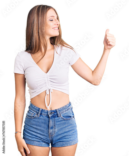 Young beautiful blonde woman wearing casual white tshirt looking proud  smiling doing thumbs up gesture to the side