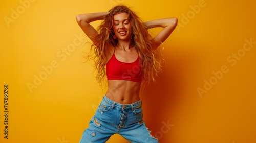 Energized happy girl raises hands joyfully, being in high spirit, dances music, has slim figure, dressed in casual clothes, poses against yellow background, jumps playfully