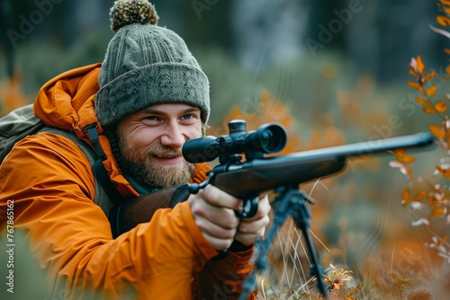 Close-up of a male hunter with a rifle in the woods. Focused young man shooter takes aim from a rifle with a telescopic sight. The hunter waits patiently for his prey in ambush.