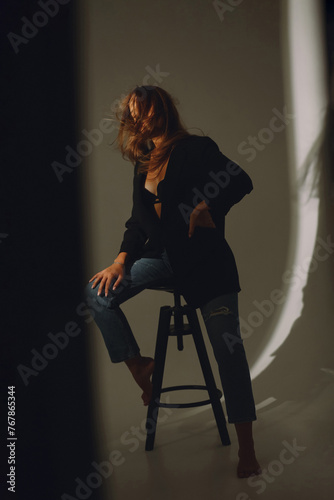 Young woman in black bra, jacket and jeans posing on a cyclorama with blowing hair