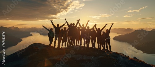 On a mountaintop, a large group of people are enjoying a success pose with their arms raised against a sunset lake and mountains. This is a concept for travel, adventure, or expedition. photo