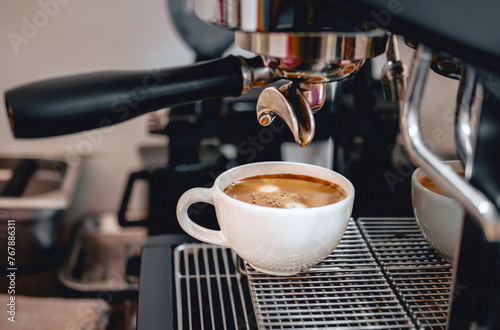 Coffee extraction from the coffee machine with a portafilter pouring coffee into a cup,Espresso poruing from coffee machine at coffee shop photo