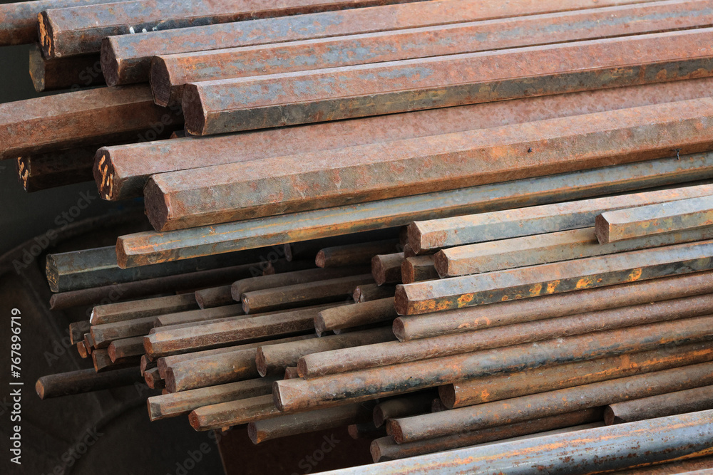 A pile of rusty metal rods. The rods are stacked on top of each other and are all different sizes. Scene is somewhat bleak and industrial, as the rods appear to be old and worn