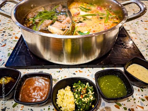 A pot of spicy soup served with many flavored dipping sauces.