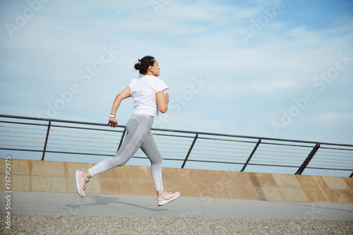 View from the back to a sportswoman, runner jogger athlete doing cardio workout, running outdoors on the city bridge