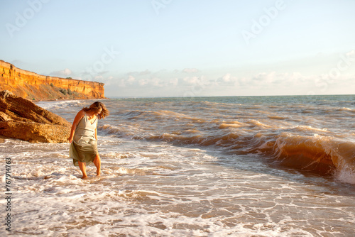 A beautiful large  in a turquoise sundress walks alonf the seashore against the sand beach and sea or ocean photo