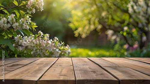 Spring beautiful background with green lush young foliage and flowering branches with an empty wooden table on nature outdoors in sunlight in garden.