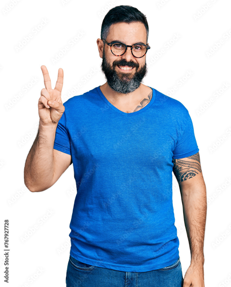 Hispanic man with beard wearing casual t shirt and glasses smiling with happy face winking at the camera doing victory sign. number two. Hispanic man with beard wearing casual t shirt and glasses smiling with happy face winking at the camera doing victory sign. number two.