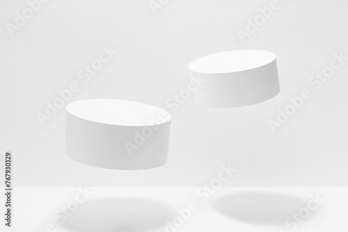 Abstract white scene mockup - two round tilt white cylinder podiums levitate in hard light, shadow. Template for presentation cosmetic products, goods, advertising, design, sale in fashion style.