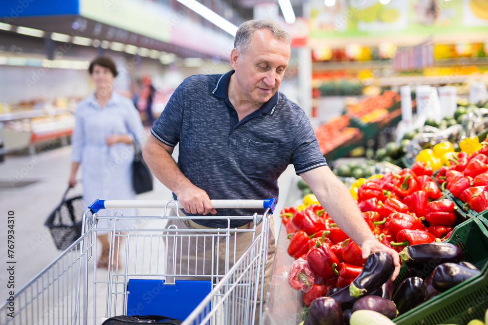 Mature man choosing eggplant in supermarket