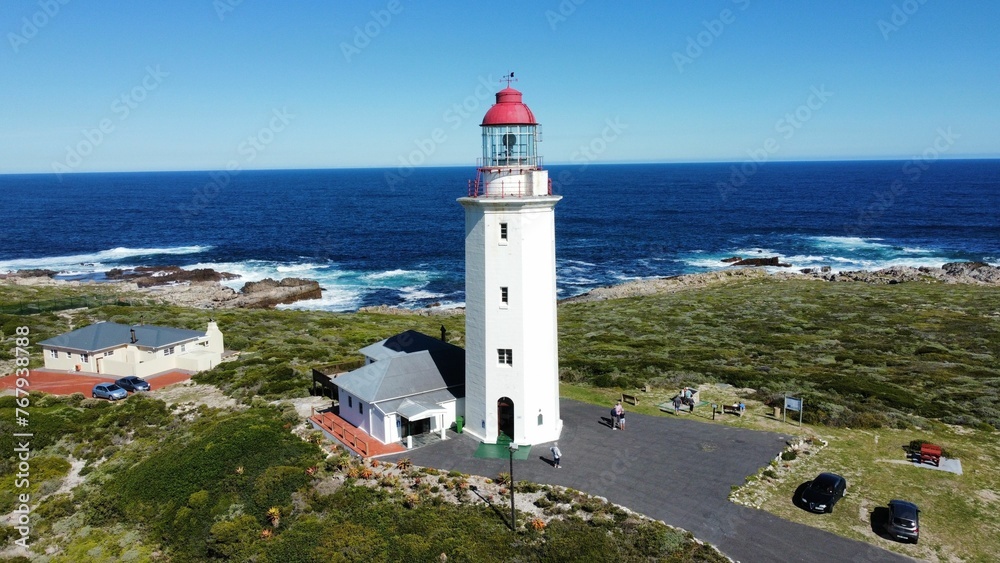 Aerial shot of a white lighthouse on the coast of a serene body of water on a sunny day