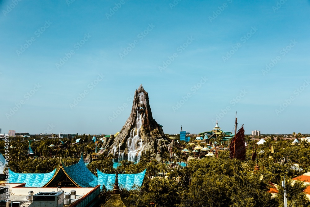 Vibrant amusement park surrounded by lush green trees and a clear blue sky: volcano bay Orlando