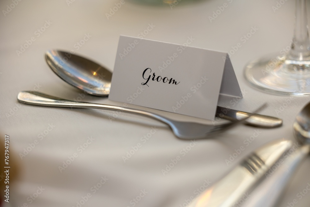 Place card is set atop a spoon and fork, both made of gleaming silver Place card is set atop a spoon and fork, both made of gleaming silver
