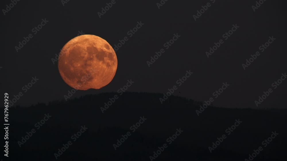 A large full moon rises above the silhouette of a mountain range against a darkening sky A large full moon rises above the silhouette of a mountain range against a darkening sky