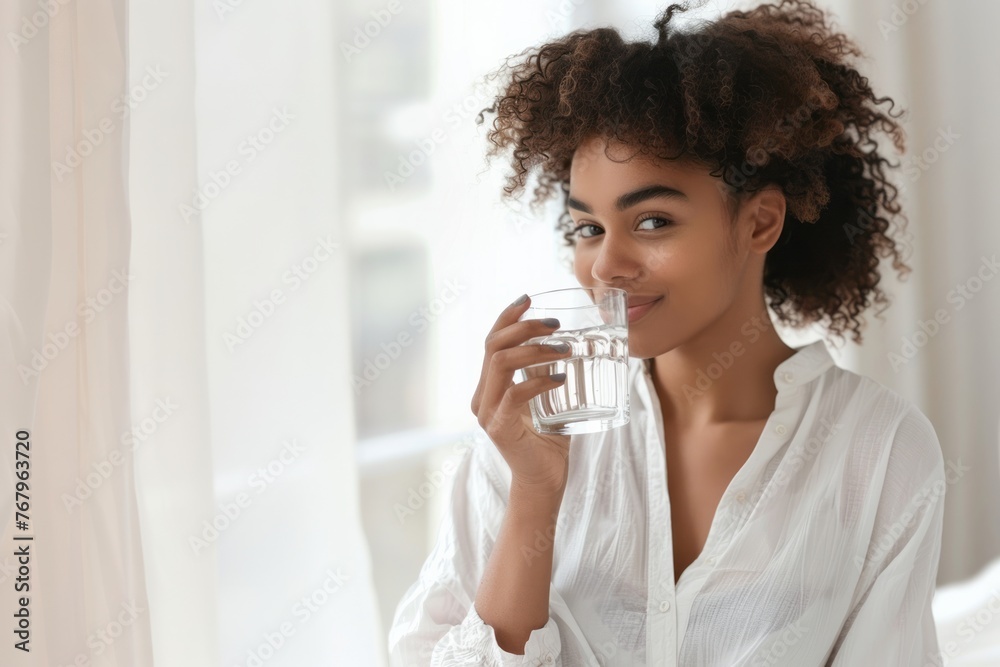 Portrait of a beautiful African American young woman drinking water standing in the kitchen at home Portrait of a beautiful African American young woman drinking water standing in the kitchen at home