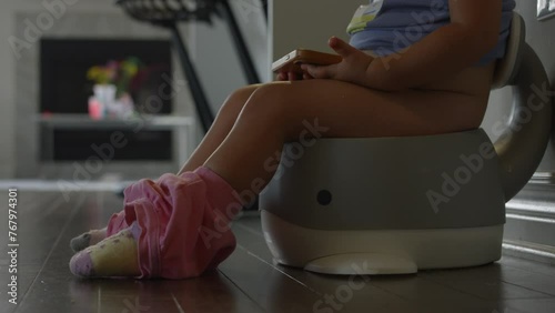 Toddler girl sits on potty watching smart phone - potty training - side profile