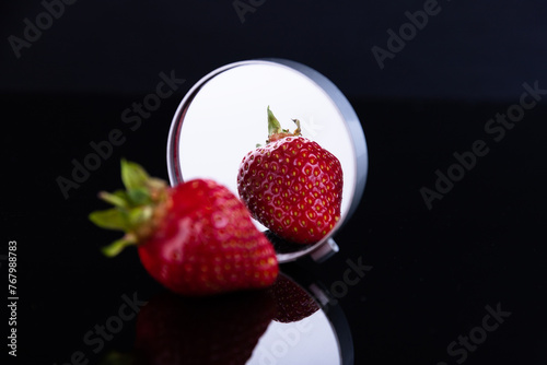Fototapeta Naklejka Na Ścianę i Meble -  Red strawberries on a black background with reflection in the mirror. The concept of beauty and perfection. Selective focus