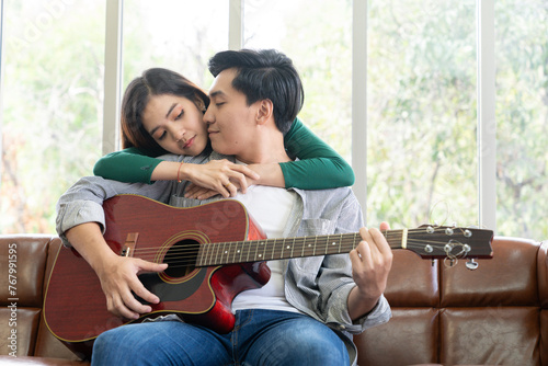 The couple, a young man and woman, are enjoying playing the guitar together at home