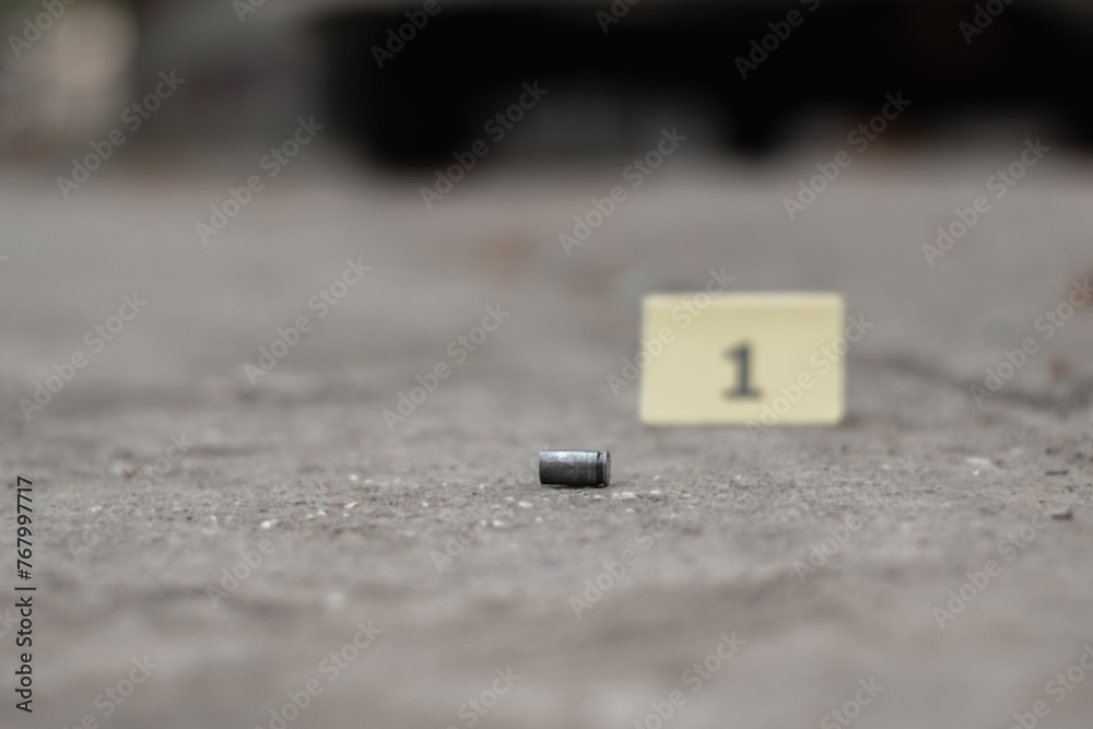 Pistol bullet shell on cement floor with blurred number one yellow paper background, concept for investigation and crime by using gun, soft focus. Pistol bullet shell on cement floor with blurred number one yellow paper background, concept for investigation and crime by using gun, soft focus.