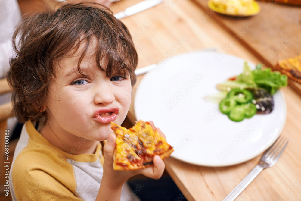 Boy, child and pizza in portrait at dinner table for eating, food and relax on holiday in family house. Kid, happy and playful in dining room for lunch with nutrition, diet and home for funny face