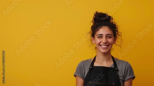 Portrait of a girl with an apron for a waiter laughing while posing on a yellow background, 