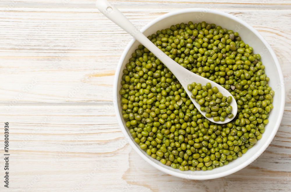 Green mung beans in a ceramic bowl with a spoon on a white wooden background. Vegan and vegetarian food. The concept of healthy eating. Horizontal orientation. Copy space. Top view. Selective focus. Green mung beans in a ceramic bowl with a spoon on a white wooden background. Vegan and vegetarian food. The concept of healthy eating. Horizontal orientation. Copy space. Top view. Selective focus.