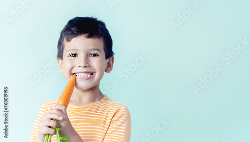 Little boy with strong teeth eats carrot on green background. Joyful toddler kid likes fresh vegetable in studio. Food for children health.