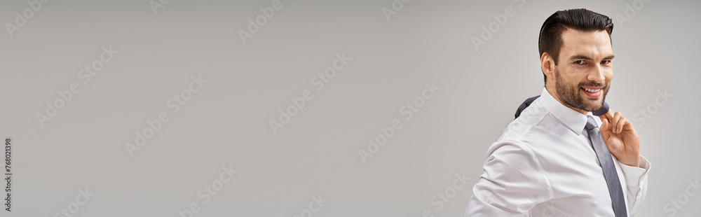 portrait of happy businessman in his 30s holding jacket over shoulder while standing on grey, banner portrait of happy businessman in his 30s holding jacket over shoulder while standing on grey, banner