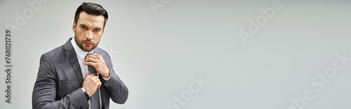 фотографія thoughtful man in formal wear adjusting tie on grey background, corporate fashio
