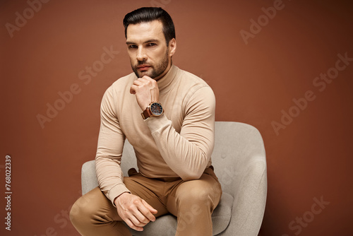 фотографія handsome and serious man with bristle sitting on comfortable armchair on beige b