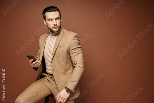 distracted businessman in elegant attire holding his smartphone on beige background, social media © LIGHTFIELD STUDIOS