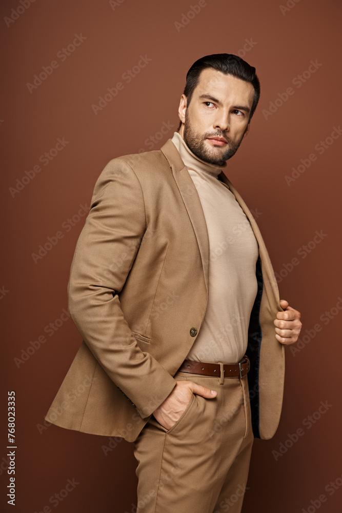 handsome man in elegant attire looking away while posing with hand in pocket on beige background handsome man in elegant attire looking away while posing with hand in pocket on beige background