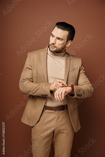 handsome man in elegant attire checking his wristwatch on beige background, time management