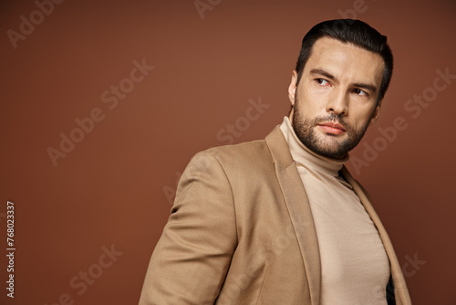 handsome man in elegant attire looking away while posing in blazer on beige background