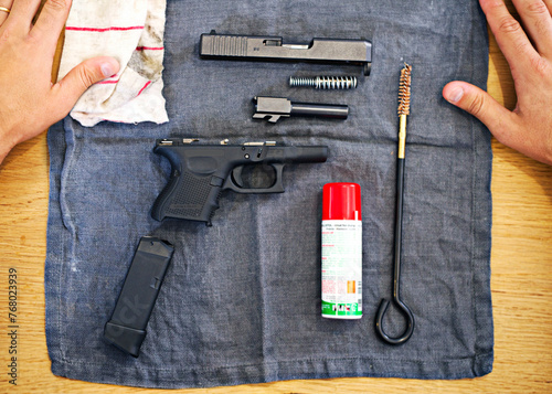 Hands, cleaning and man with gun on cloth for safety, self defense and handgun assembly. Process, equipment and person with firearm maintenance, magazine and metal parts to assemble weapon on table