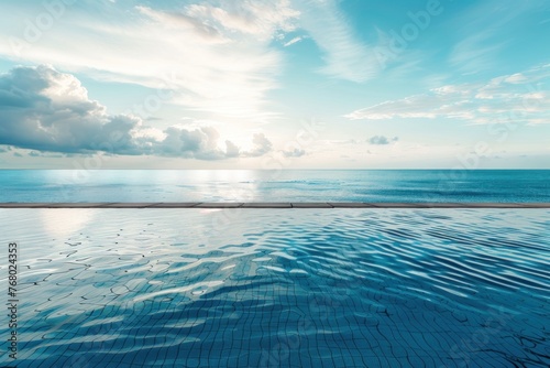 Blue water in a swimming pool with a beautiful seascape of the ocean and blue sky with white clouds on the background