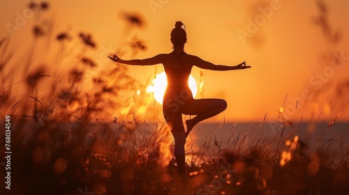 A silhouette of a person in a yoga pose during a vibrant sunset, surrounded by tall grass, exuding peace and mindfulness.