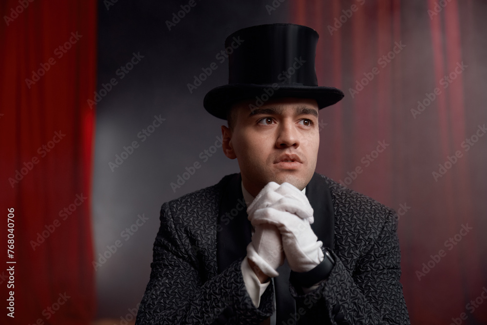 Magician wearing top hat and tuxedo suit holding magic cards in hands