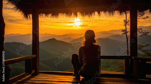 Young woman sitting on the wooden terrace with beautiful sunrise in the morning .